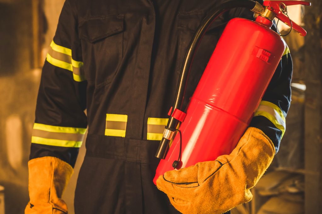 Firefighter in brown jacket with reflective yellow stripes holding a red fire extinguisher.
